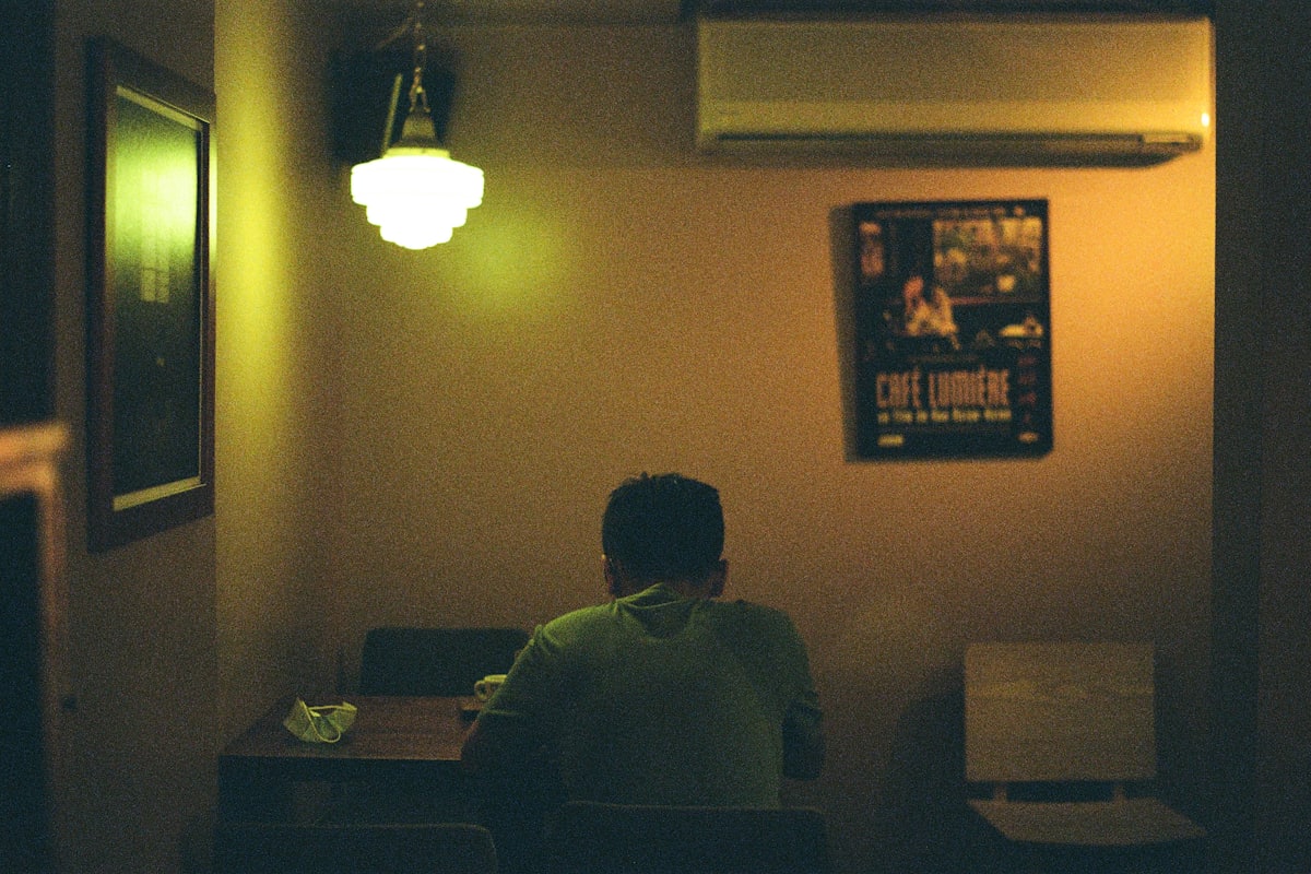 Two people sitting apart in a kitchen at night, the distance between them visible
